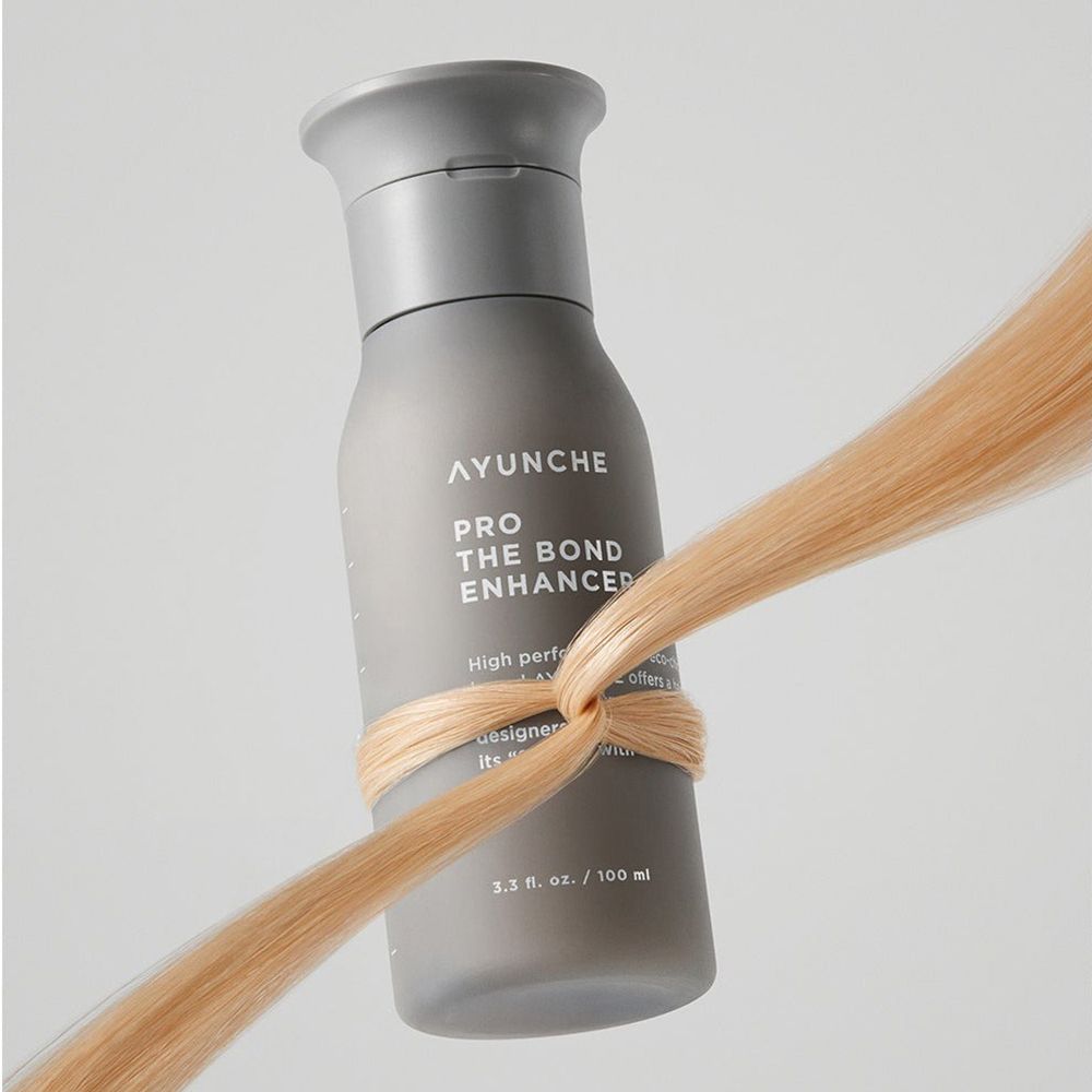 Graue Flasche mit AYUNCHE PRO THE BOND ENHANCER. Blonde Haarsträhne umwickelt die Flasche.
