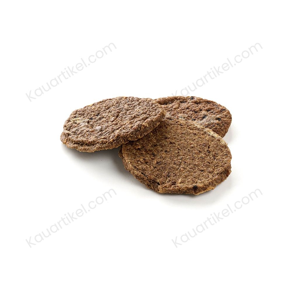 Hund kaut auf einem Pferde-Burger Leckerli, drei weitere liegen auf einem Holzstamm.
