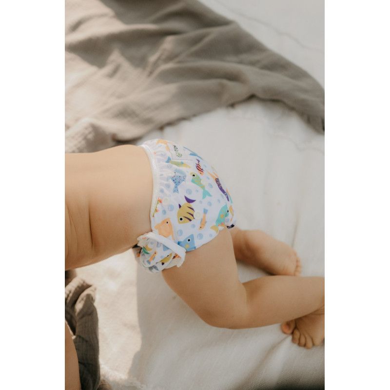 Baby trägt Schwimmwindel mit Fischmuster. Kind liegt auf einer Decke. Die Windel bedeckt den Po.