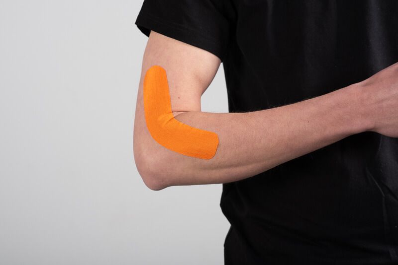 Orangefarbenes Kinesiotape am Ellenbogen einer Person angebracht.