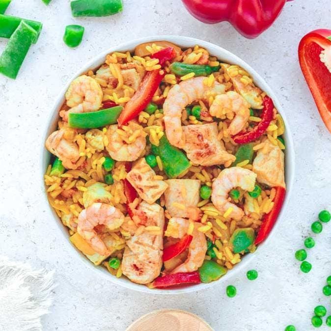 Reisgericht mit Garnelen, Hähnchen und Gemüse. Draufsicht. Auf hellem Untergrund. Garnelen, Erbsen, Paprika.