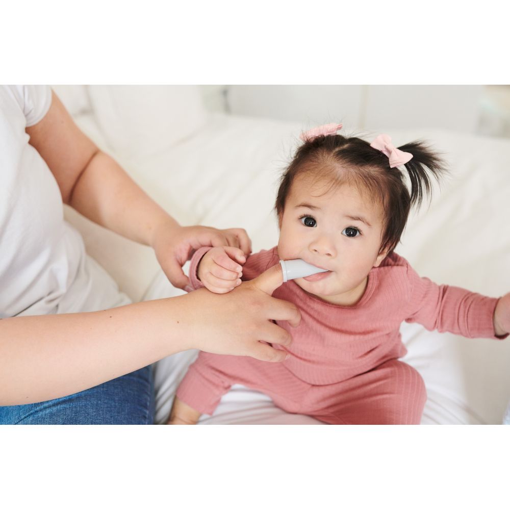 Baby mit Fingerzahnbürste im Mund. Person hält die Bürste. Baby trägt rosa Kleidung.