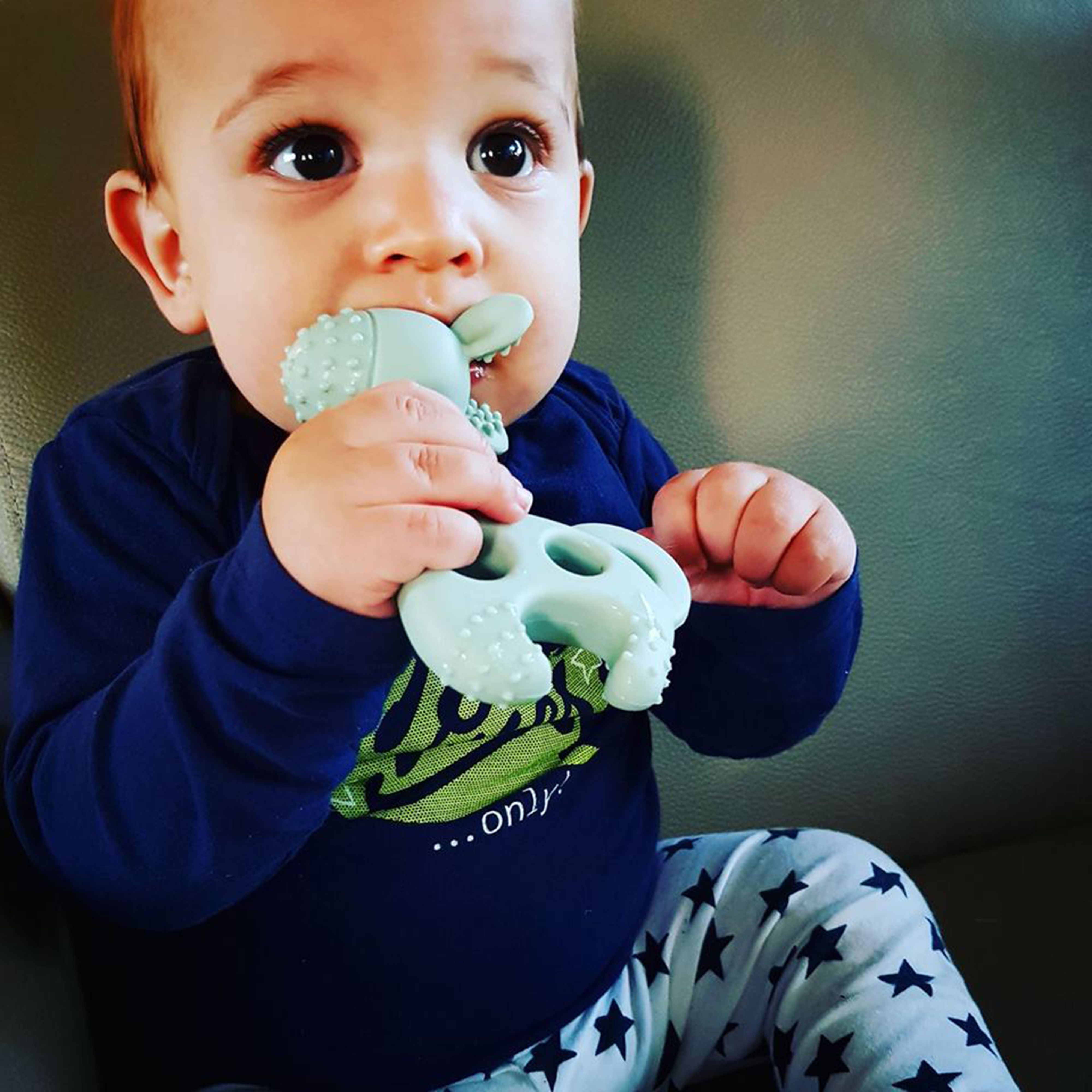 Baby mit einem grünen Beißring in Giraffenform im Mund. Das Produkt hat Noppen.