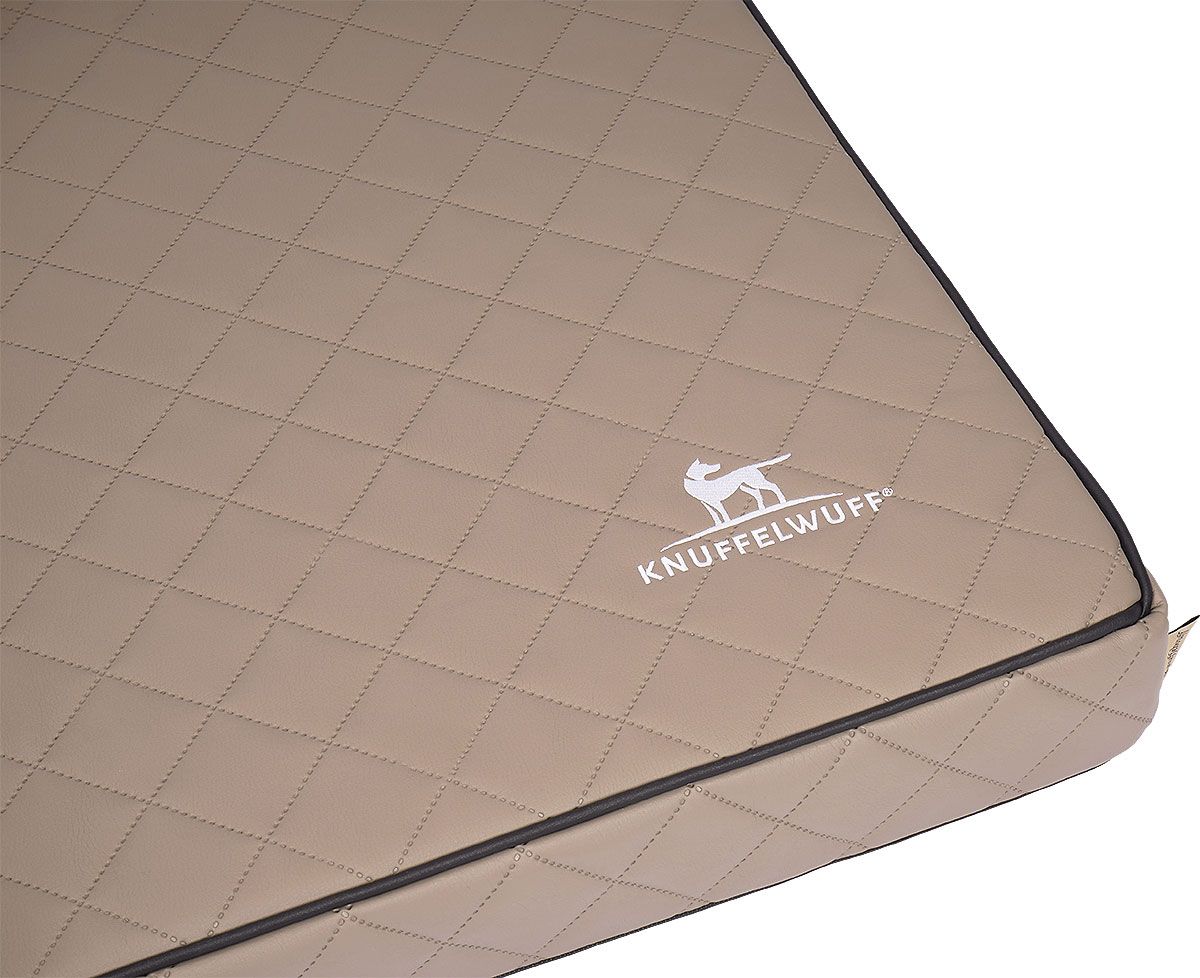 Nahaufnahme einer beigen, gesteppten orthopädischen Hundematte mit Logo und schwarzem Rand.