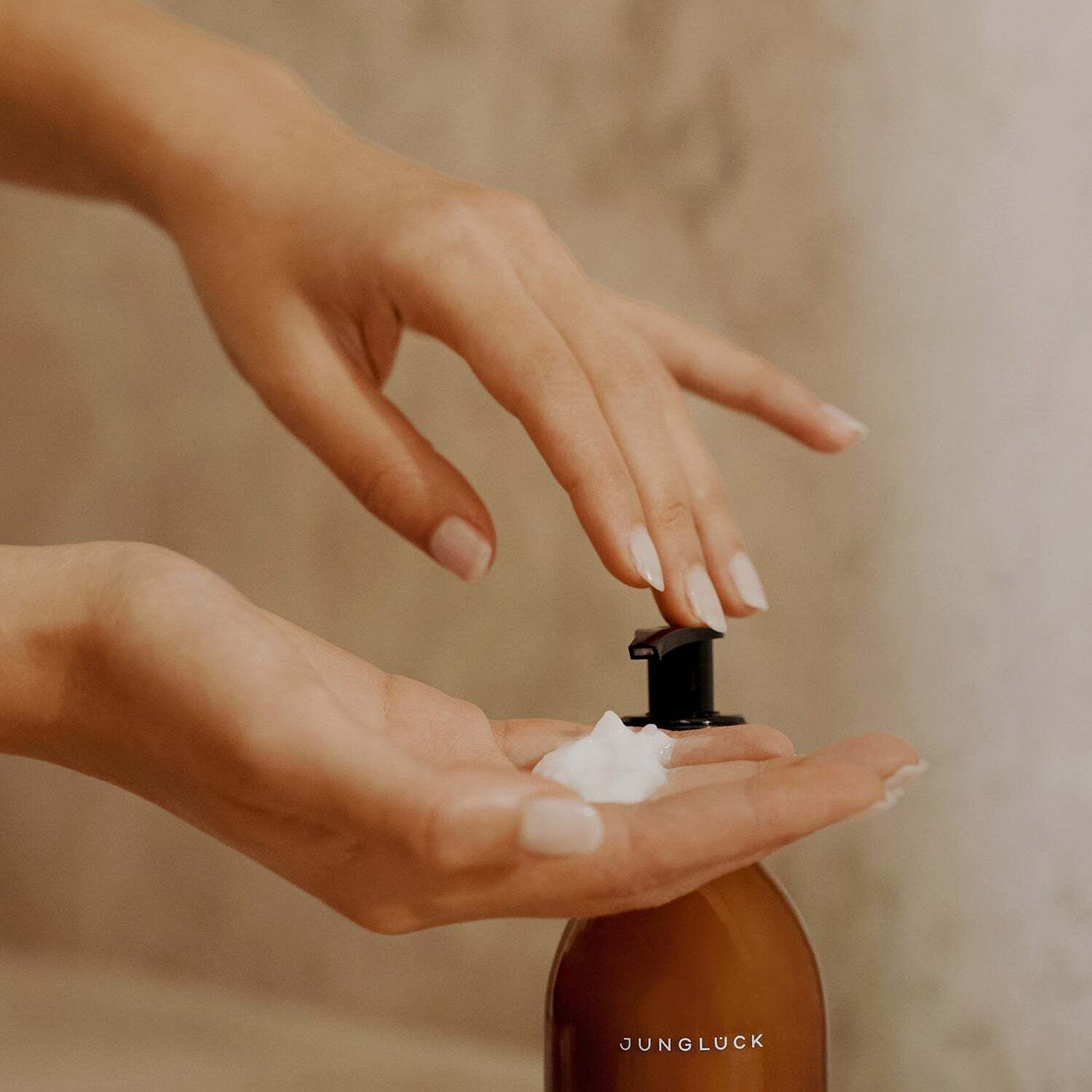 Hände halten Flasche und entnehmen Conditioner. Schwarzer Pumpverschluss. Produkt: JUNGLÜCK. Creme auf der Handfläche.