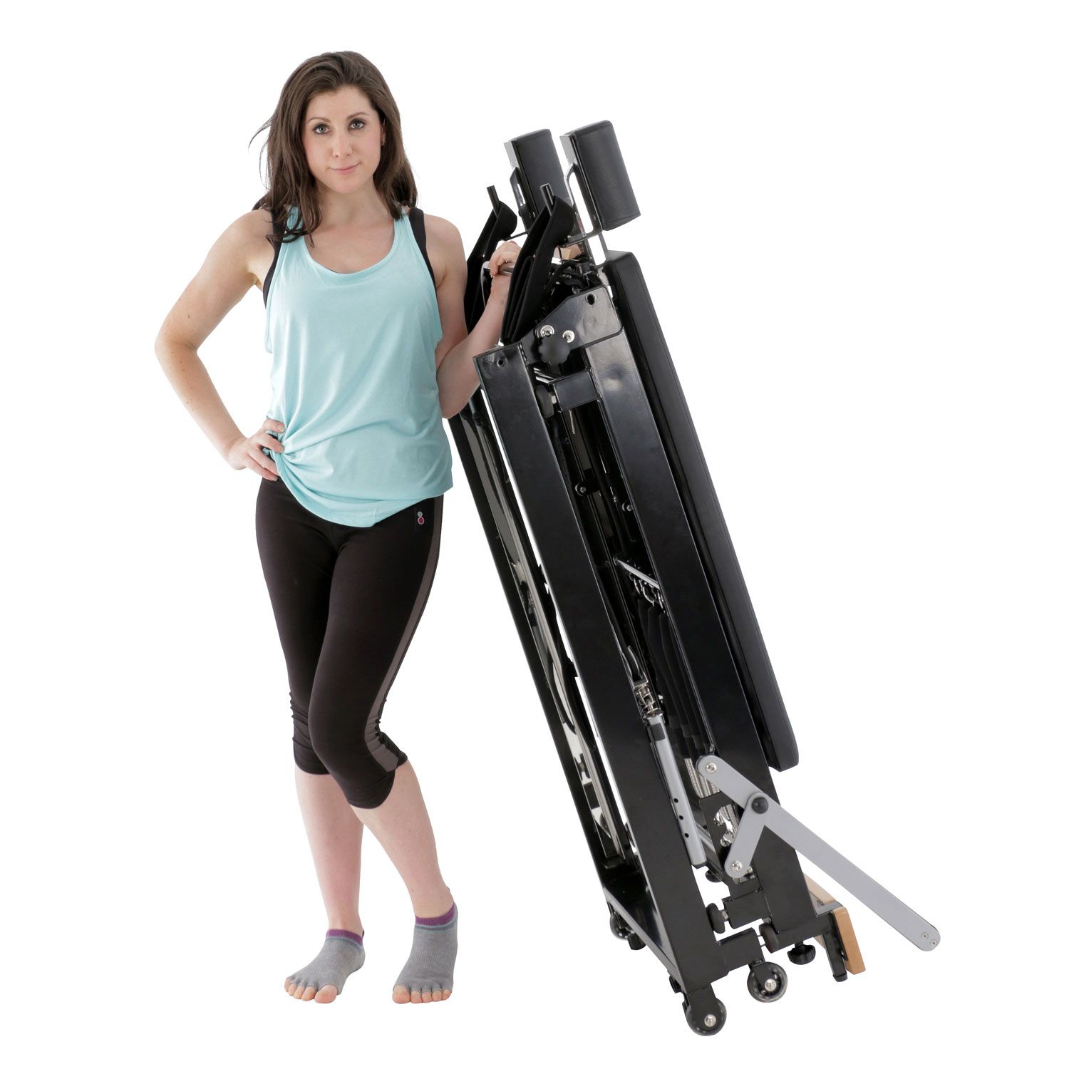 Frau steht neben einem zusammengeklappten schwarzen Pilates-Reformer. Sie trägt Sportkleidung.