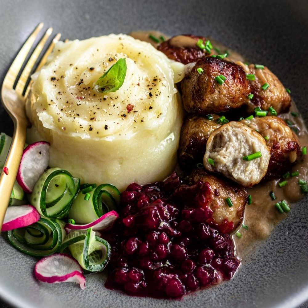 Teller mit Köttbullar, Kartoffelpüree, Preiselbeeren und Gurkensalat. Goldene Gabel.