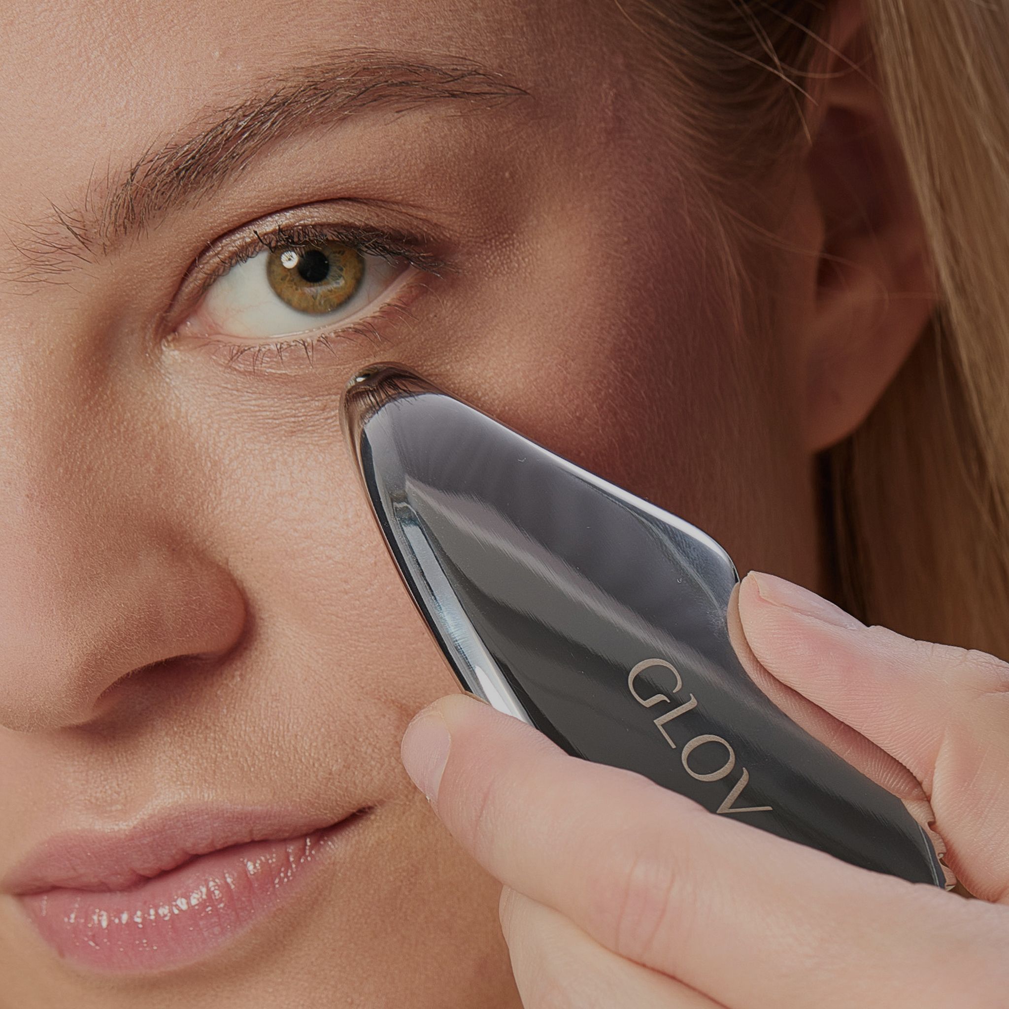 Frau wendet ein Gua Sha Werkzeug unter dem Auge an. Das Werkzeug ist schwarz und glänzend.