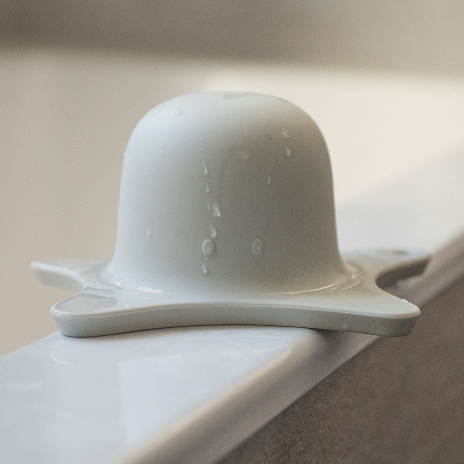 Hellgraue Duschhilfe auf einer weißen Oberfläche. Wasser tropft von der runden Oberseite. Sternförmige Basis.