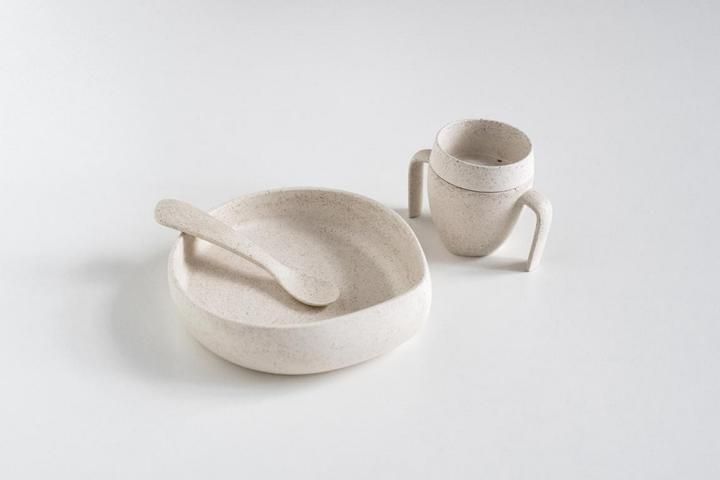 Beige Geschirr-Set: Schüssel, Löffel und Becher mit Henkeln. Auf weißem Hintergrund.