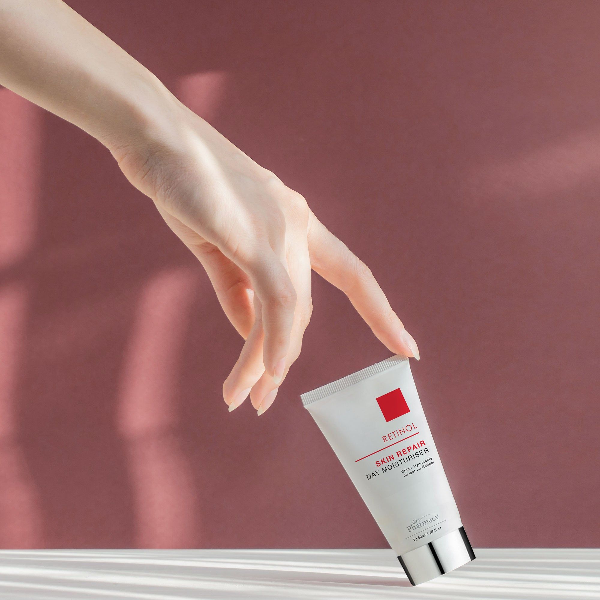 Weiße Tube mit rotem Quadrat und Aufschrift Retinol Skin Repair Day Moisturiser. Hand greift nach Tube.