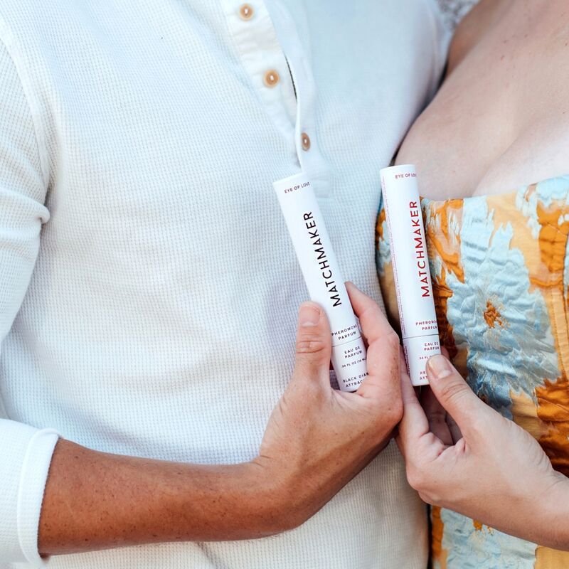 Zwei weiße Stifte mit schwarzer Schrift. Aufschrift: MATCHMAKER, Pheromon-Parfüm. Hände halten die Stifte.
