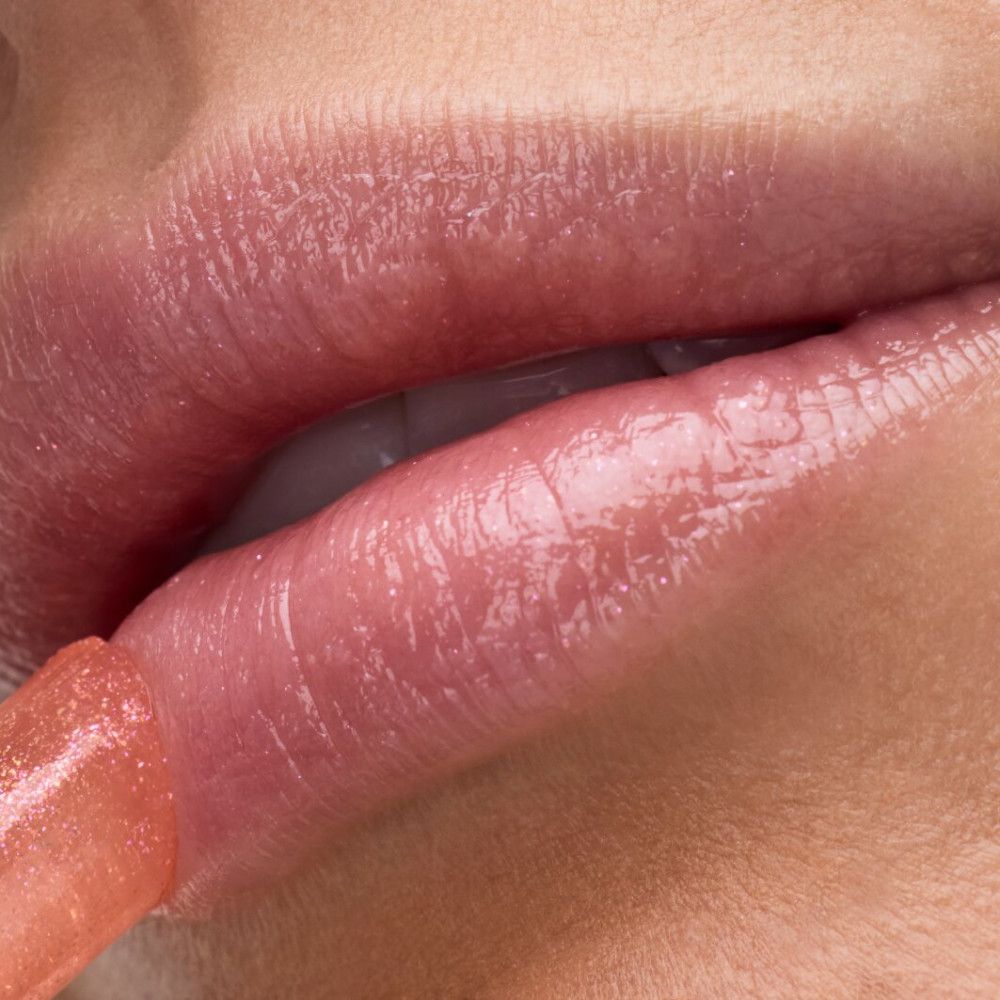 Nahaufnahme von Lippen, auf denen Lippenbalsam aufgetragen wird. Glänzendes, rosafarbenes Finish.