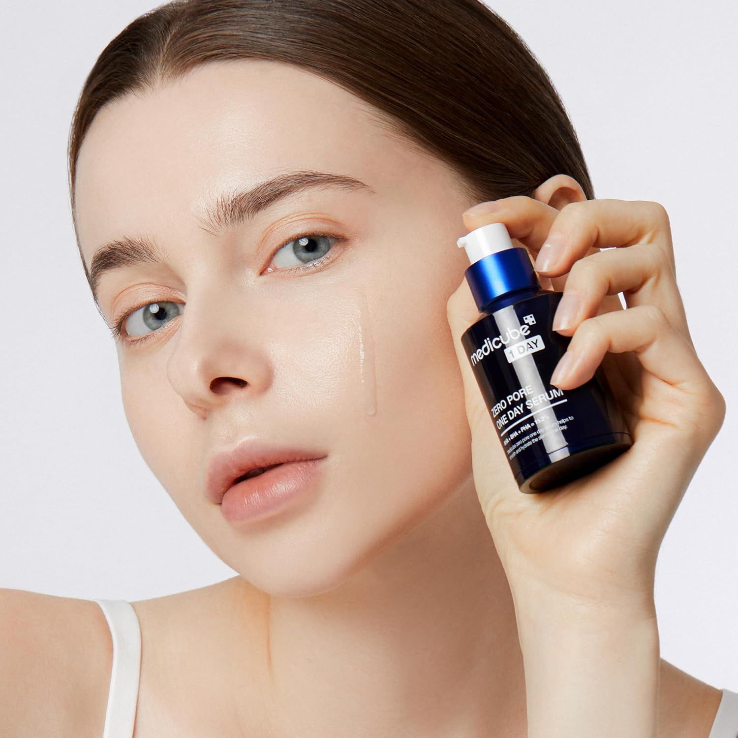 Frau hält eine Flasche MEDICUBE Zero Pore One-Day Serum. Serum auf der Haut. Blaue und weiße Flasche.