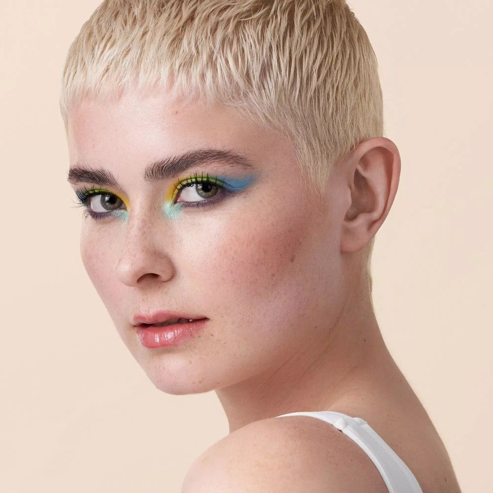 Porträt einer Frau mit kurzem, blondem Haar und farbigem Augen-Make-up. Blick zur Seite.