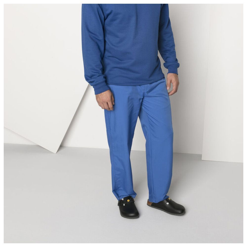 Person trägt schwarze Pantoletten. Blaue Hose und Oberteil. Schuhe mit gelbem ESD-Logo.