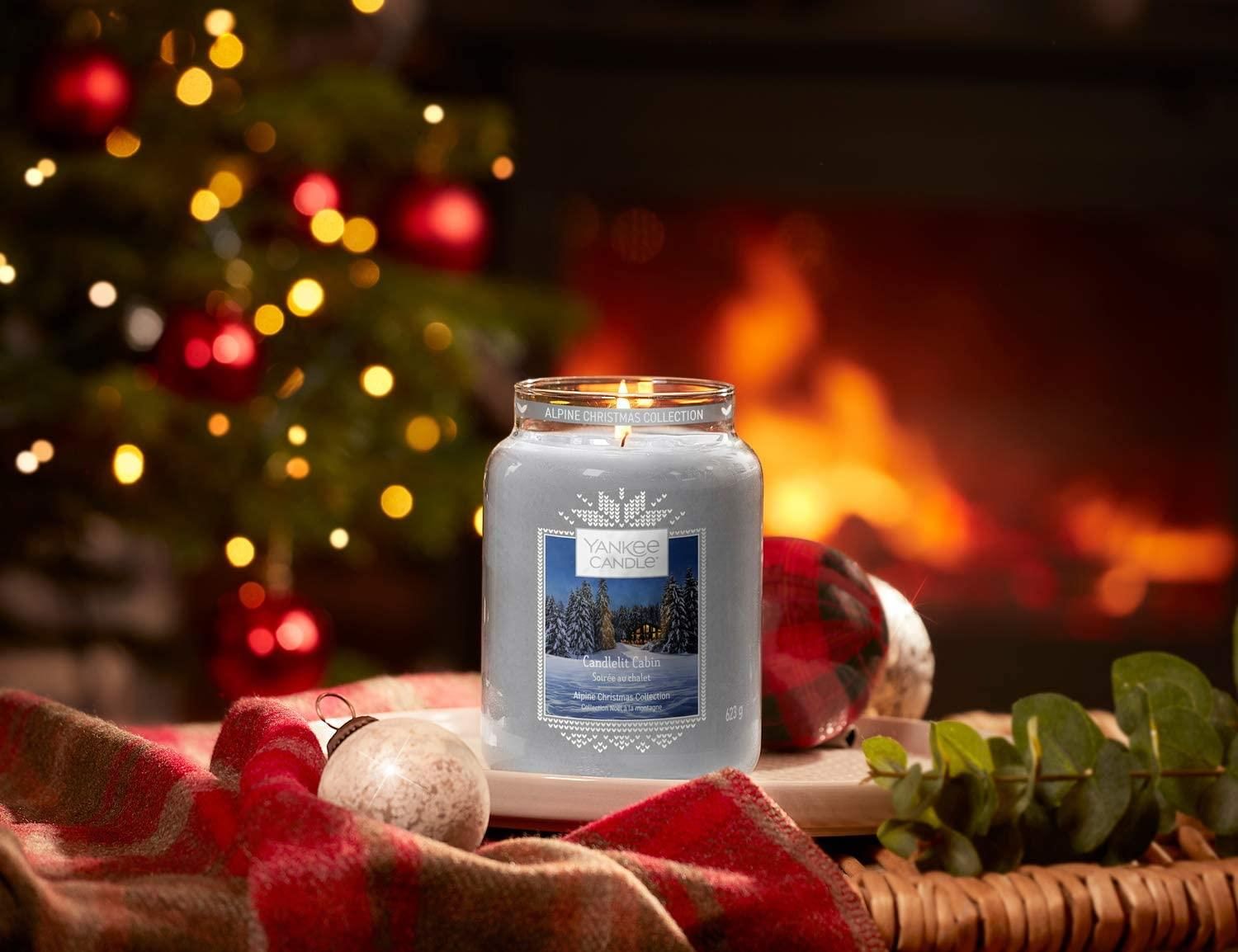 Kerzenglas mit Etikett, Winterlandschaft. Weihnachtsbaum im Hintergrund. Flamme brennt.