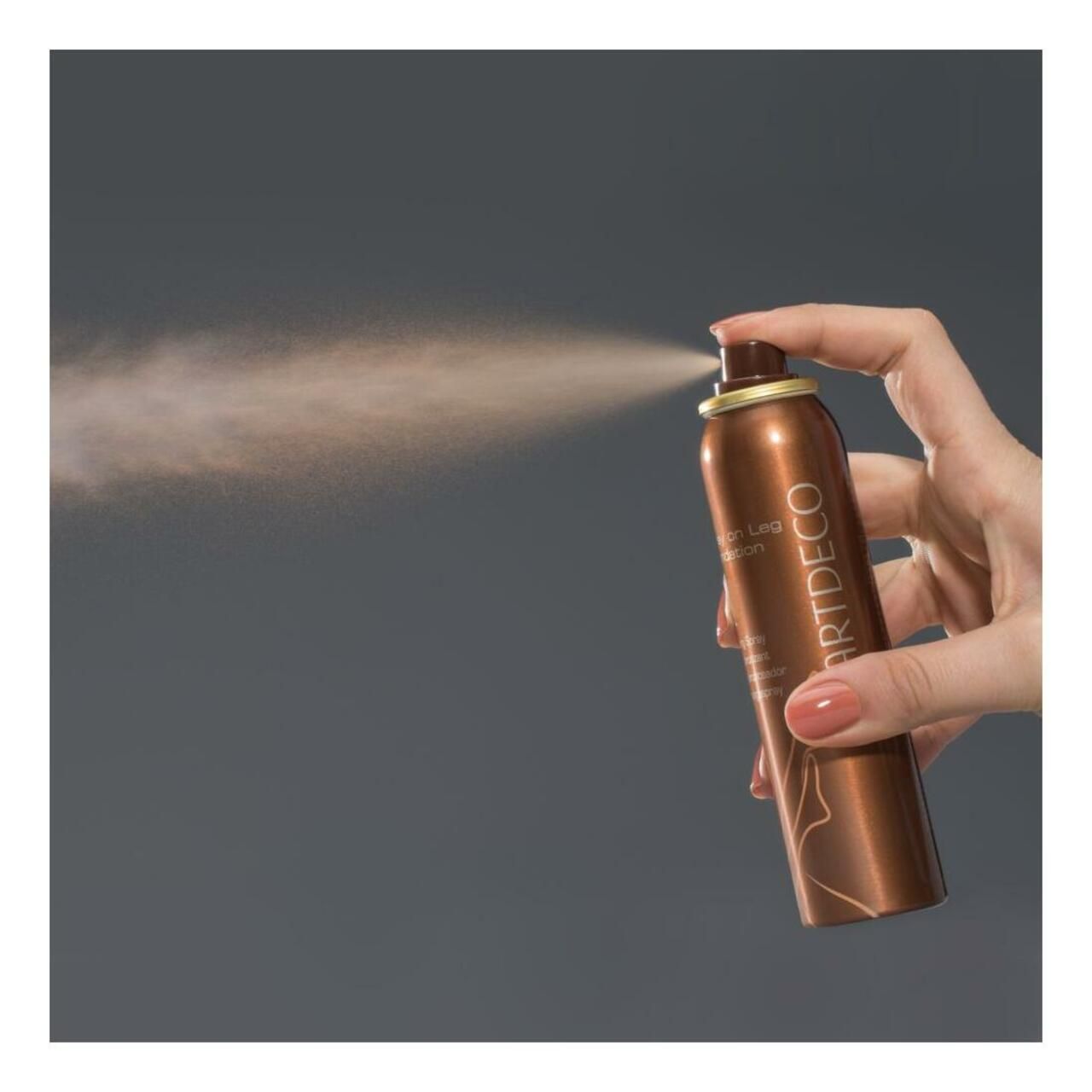 Artdeco Spray on Leg Foundation wird versprüht. Braune Sprühflasche in einer Hand. Sprühnebel sichtbar.