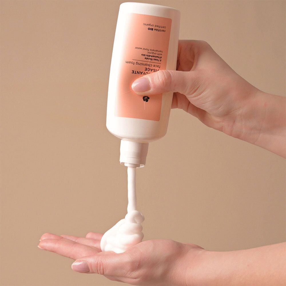 Eine Hand hält eine weiße Flasche mit einem Spender, aus dem Schaum auf die andere Handfläche gesprüht wird.