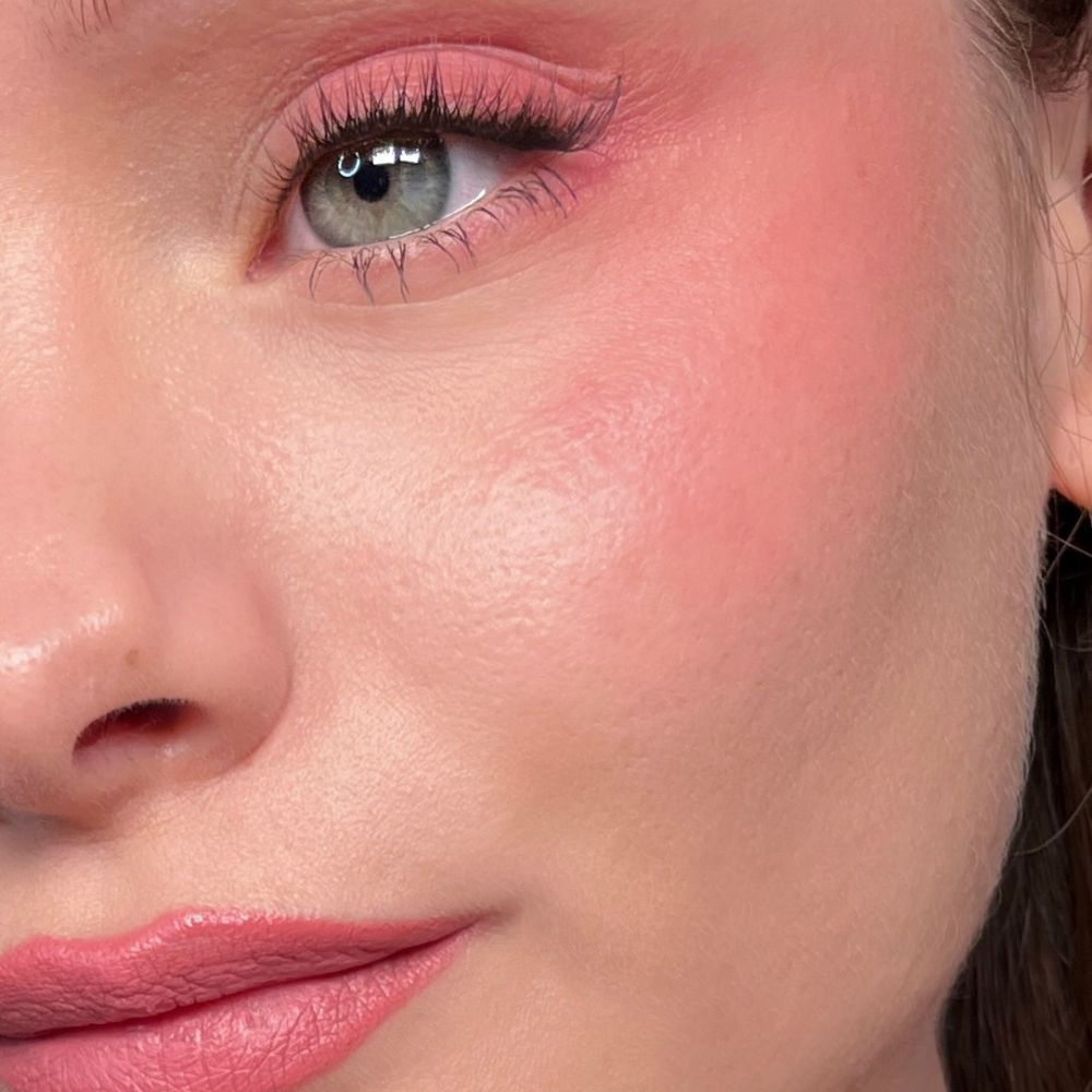 Nahaufnahme eines Gesichts mit rosa Make-up auf Augen, Wangen und Lippen. Grüne Augen.