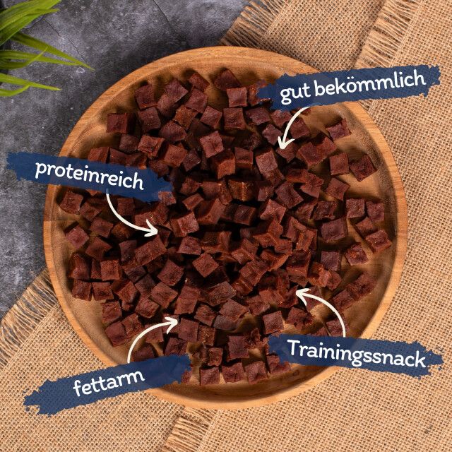 Braune, würfelförmige Snacks auf einem Holzbrett. Beschriftungen: proteinreich, fettarm, gut bekömmlich, Trainingssnack.