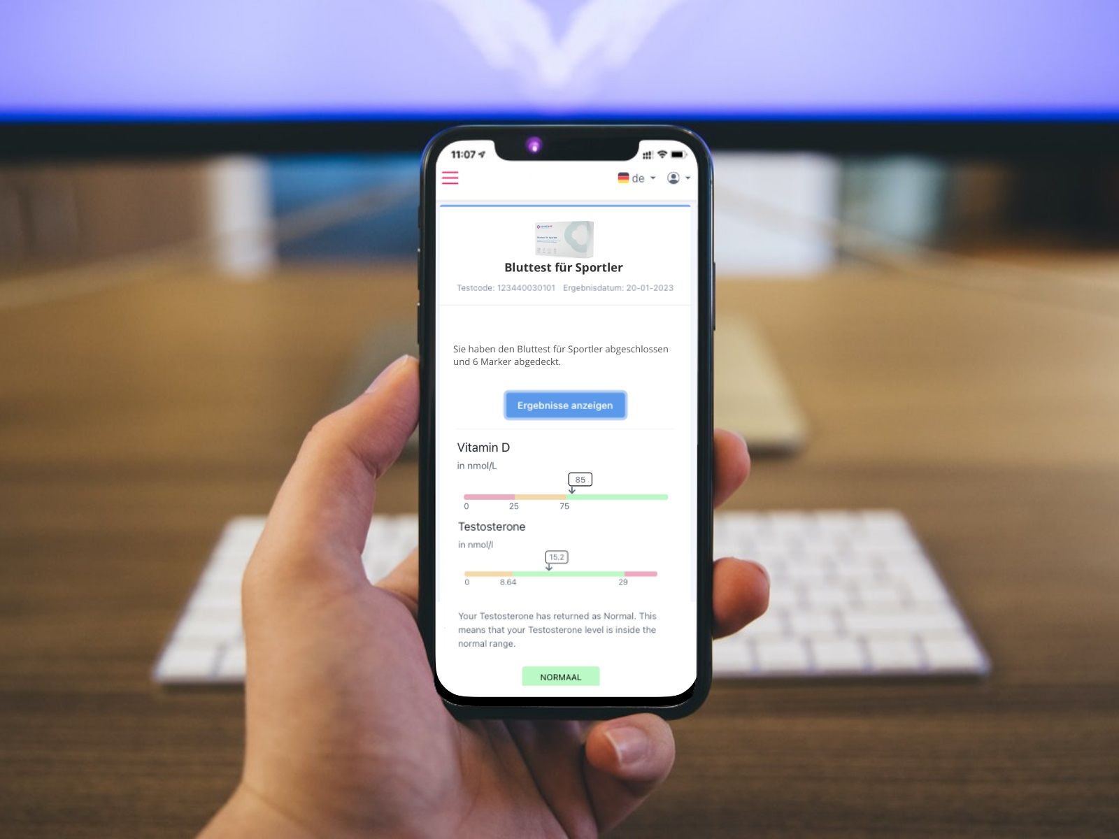 Smartphone mit Testergebnissen. Anzeige von Vitamin D und Testosteron-Werten. Hintergrund: Schreibtisch mit Tastatur.
