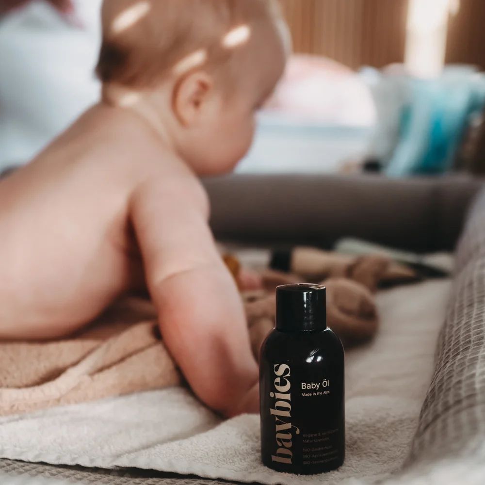 Baybies Baby Öl Flasche neben einem Baby auf einer Decke.