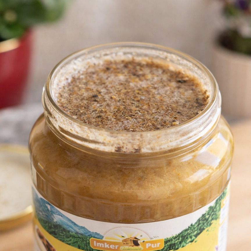 Nahaufnahme eines Glases mit Honig und Propolis. Die Oberfläche ist körnig und von dunkler Farbe.