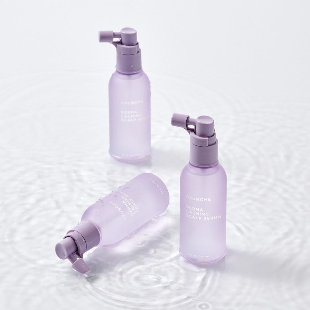 Drei durchsichtige Flaschen mit Lavendel-Applikator für Kopfhautserum, auf Wasser liegend.