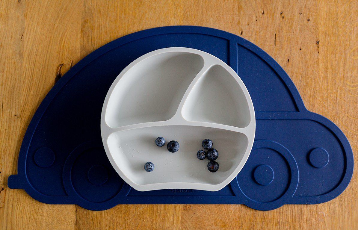 Weißer Teller mit drei Fächern auf blauem Untersetzer in Autoform, mit Blaubeeren.