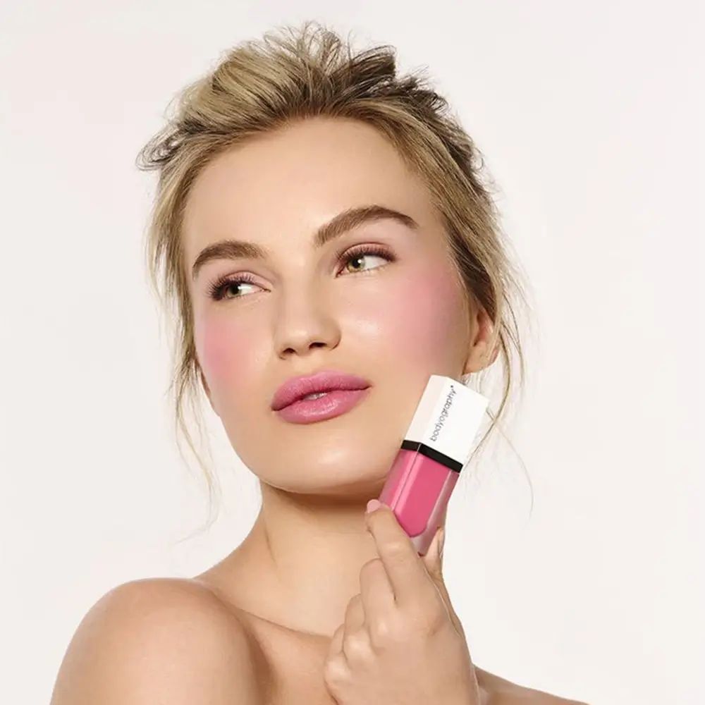 Frau mit rosa Rouge auf den Wangen. Hält ein Produkt von BODYOGRAPHY. Rosa Farbton.