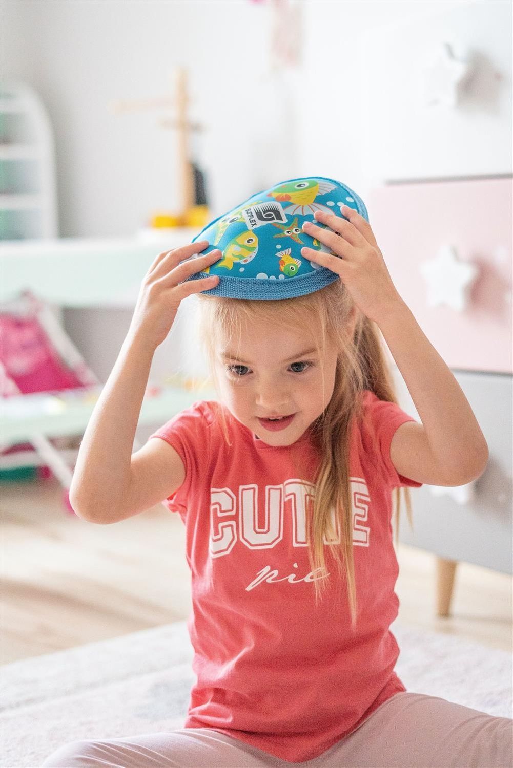 Kind setzt Sunflex Uranus Youngster Seaworld auf den Kopf. Blau mit Fisch- und Seestern-Motiven. Kind sitzt.