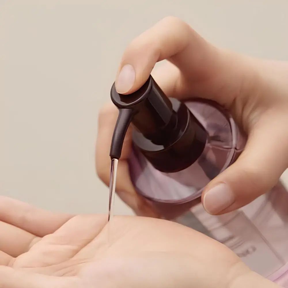 Hände drücken Flüssigkeit aus einer Flasche. Schwarze Pumpe, transparente Flüssigkeit.