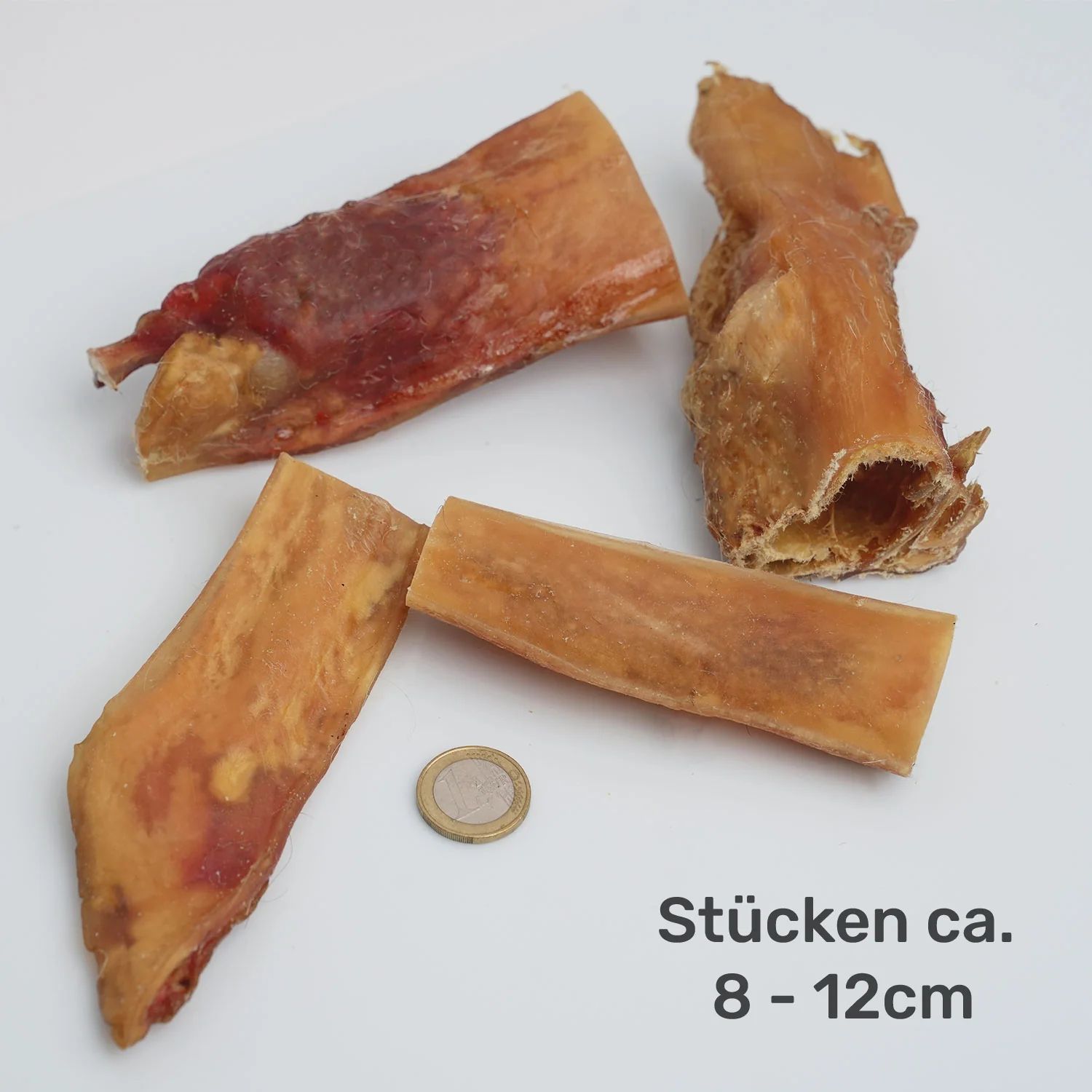 Nahaufnahme von getrockneten Rinderkopfhaut-Kauplatten. Verschiedene Formen und Größen. Münze als Größenvergleich. Text: Stücken ca. 8-12cm.