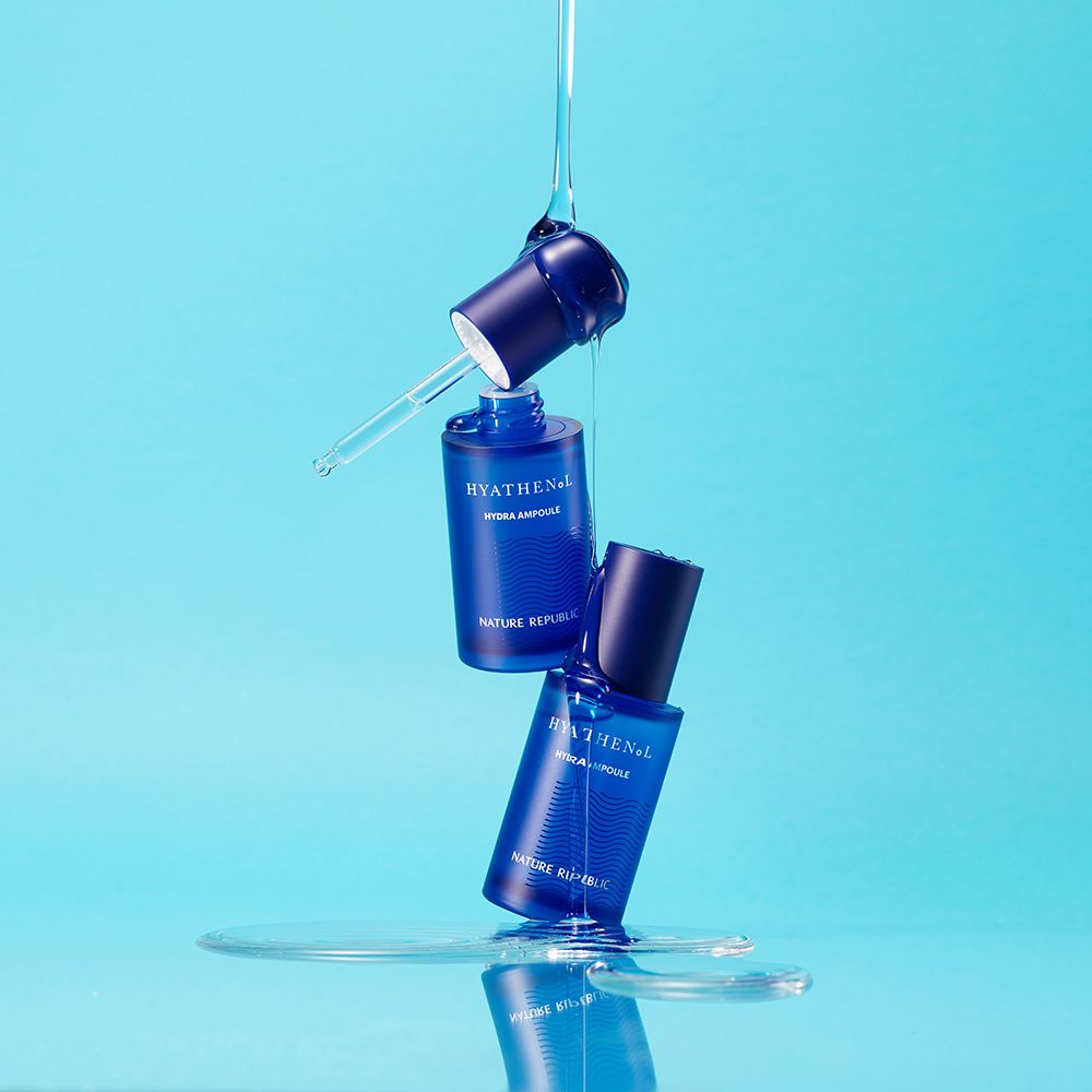Zwei blaue Serumflaschen mit Schriftzug HYATHENOL, Hydra Ampoule und NATURE REPUBLIC. Tropfen Wasser.