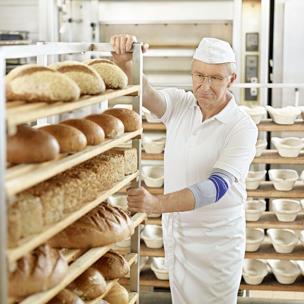 Bäcker mit Elbogenbandage schiebt einen Wagen mit Brot. Arbeitsumgebung.