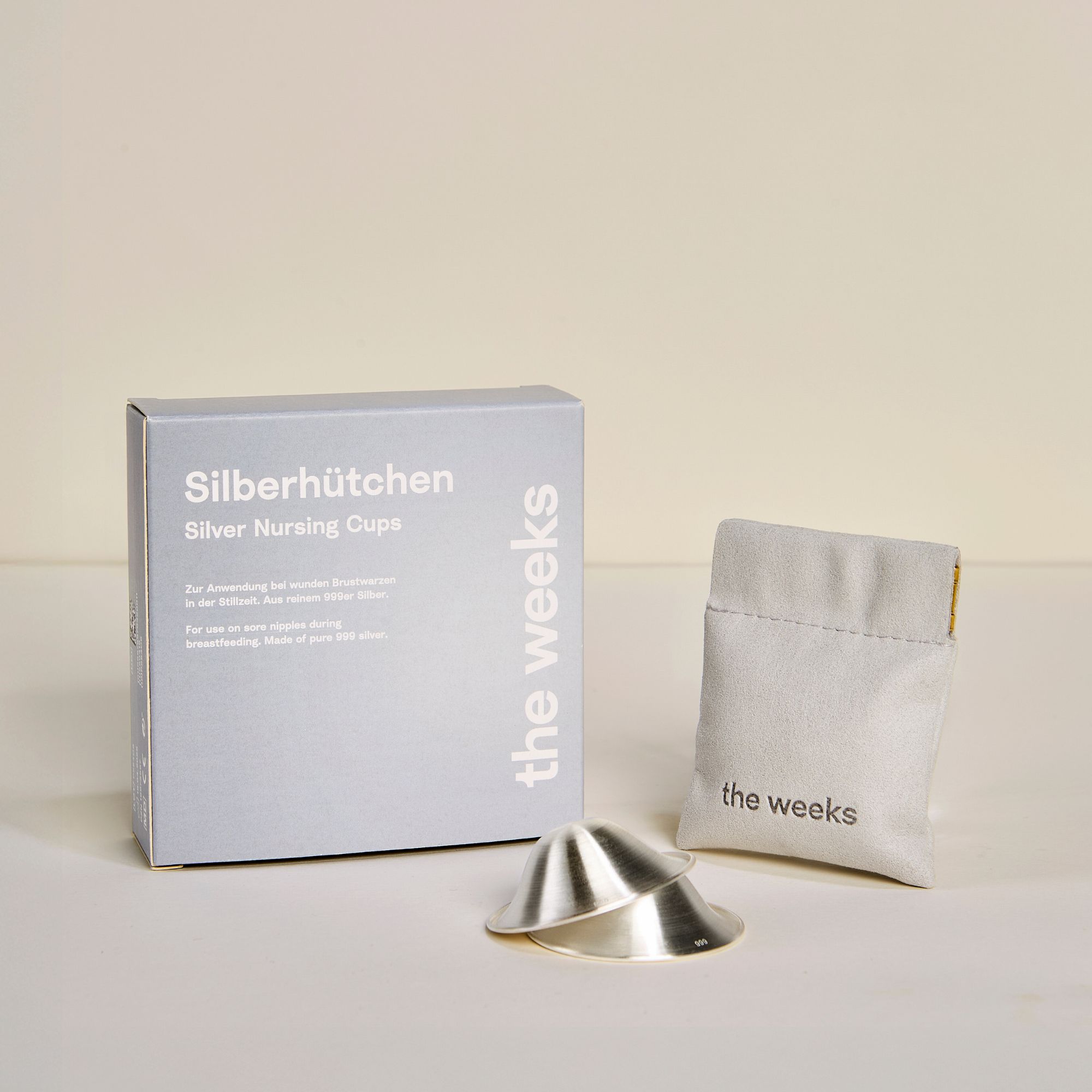 Zwei silberne Stillhütchen, Produktverpackung und Beutel. Verpackung mit Produktname und Logo.