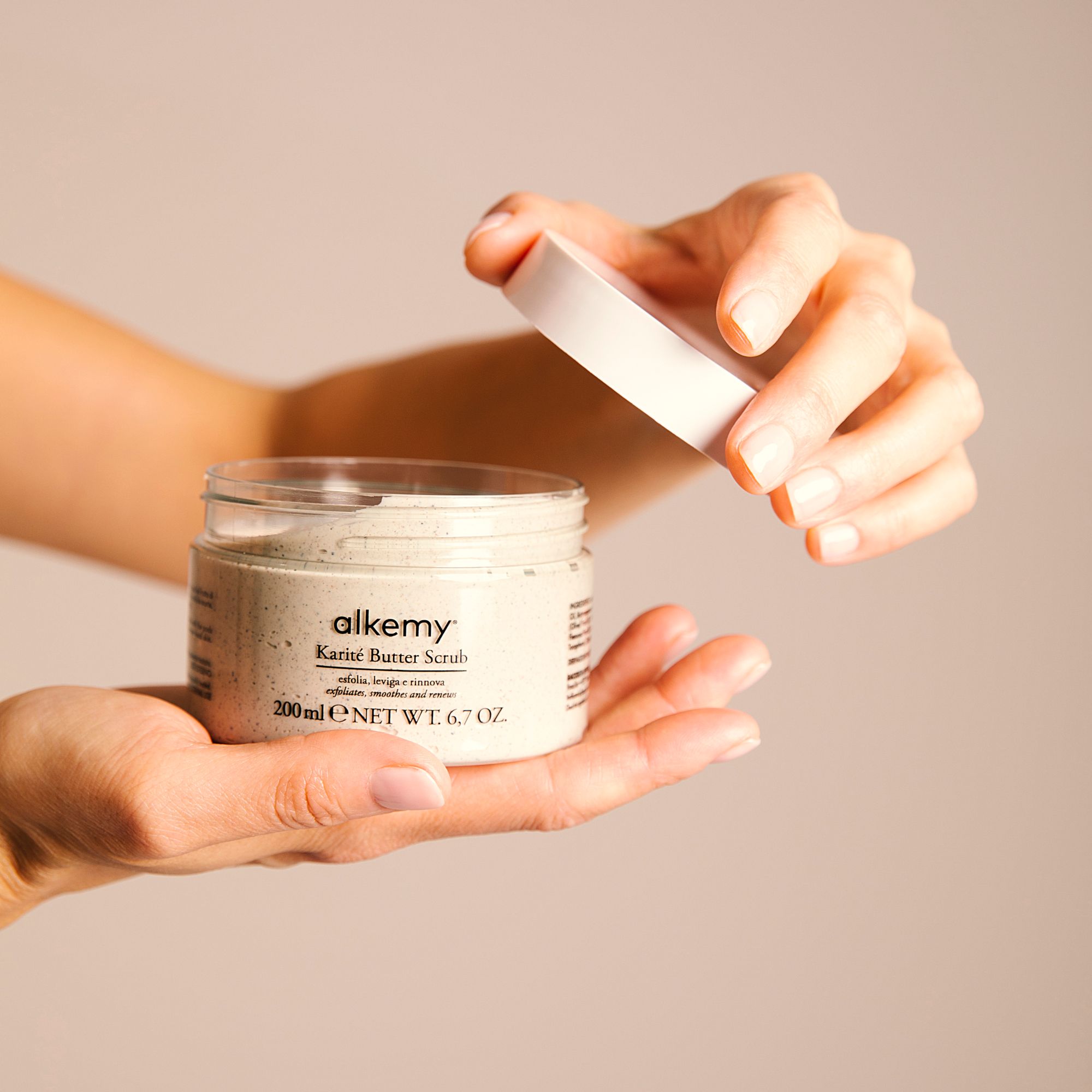 Alkemy Karité Butter Scrub Körperpeeling in einem Glasbehälter, Deckel wird geöffnet.