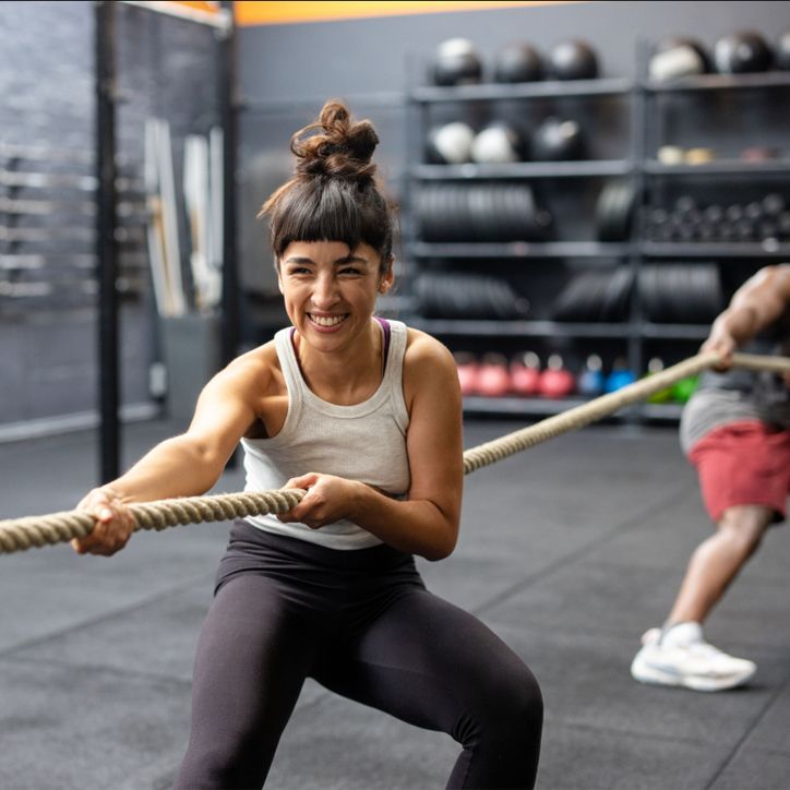 Frau zieht an einem Seil in einem Fitnessstudio. Sie lächelt und ist angespannt.