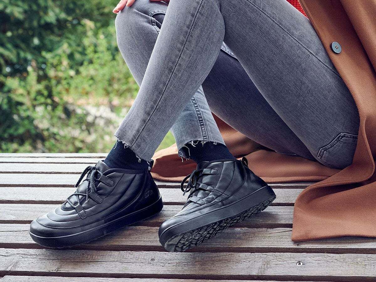 Person trägt schwarze BÄR Stiefeletten. Leder, Schnürung, breite Sohle. Ansicht von der Seite, im Freien.