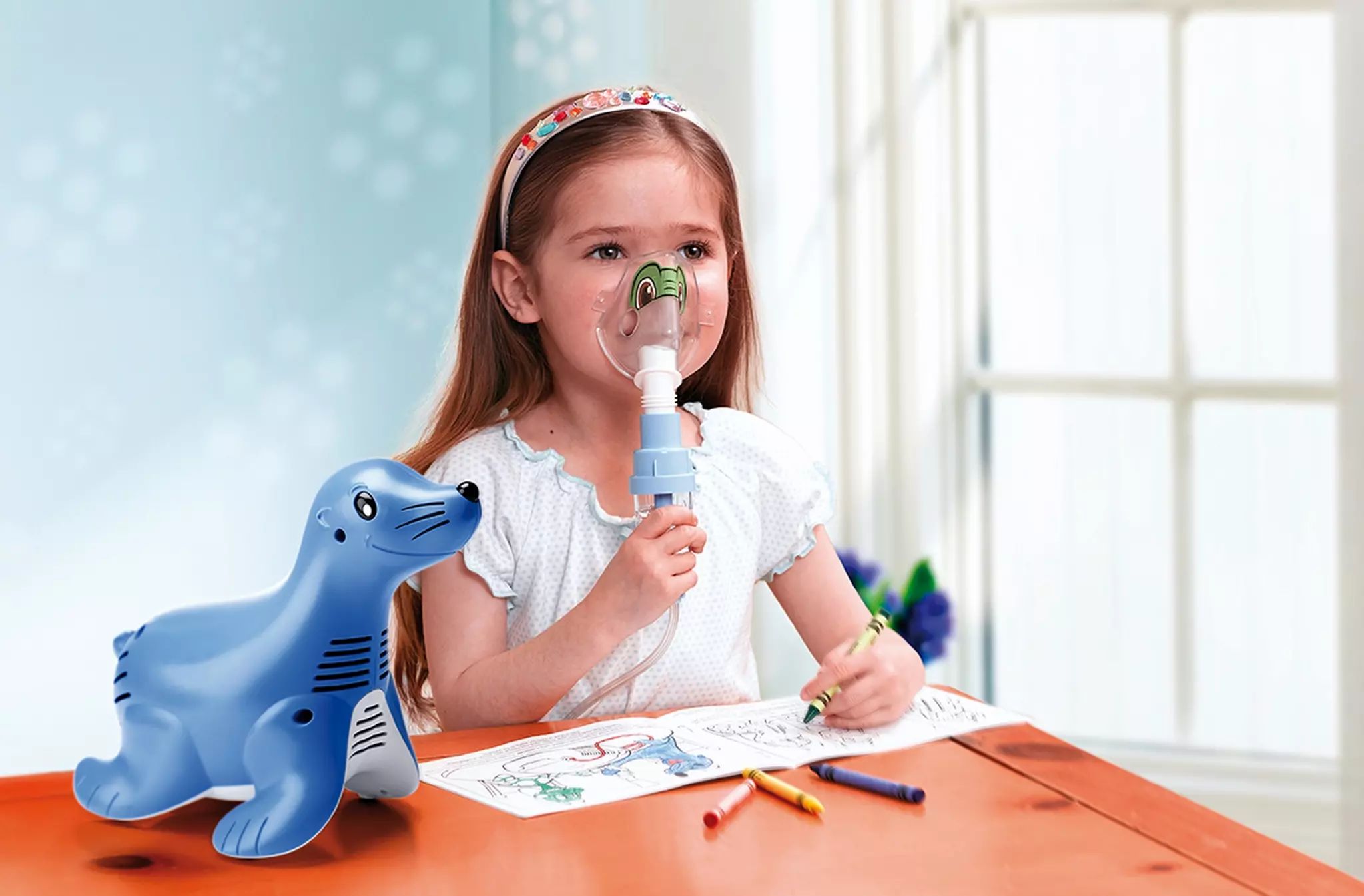 Kind mit Maske, Inhalationsgerät in Seehundform auf Tisch. Kind zeichnet, Stifte liegen bereit.