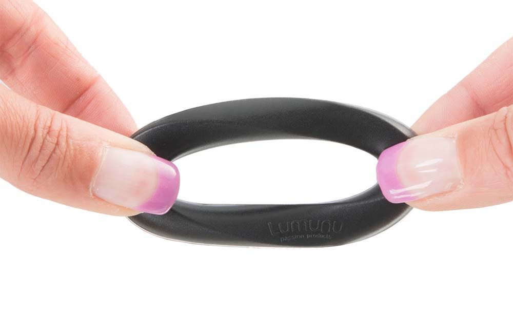 Ein schwarzer Silikon-Cockring wird zwischen zwei Händen gehalten. Der Ring ist leicht gedehnt.