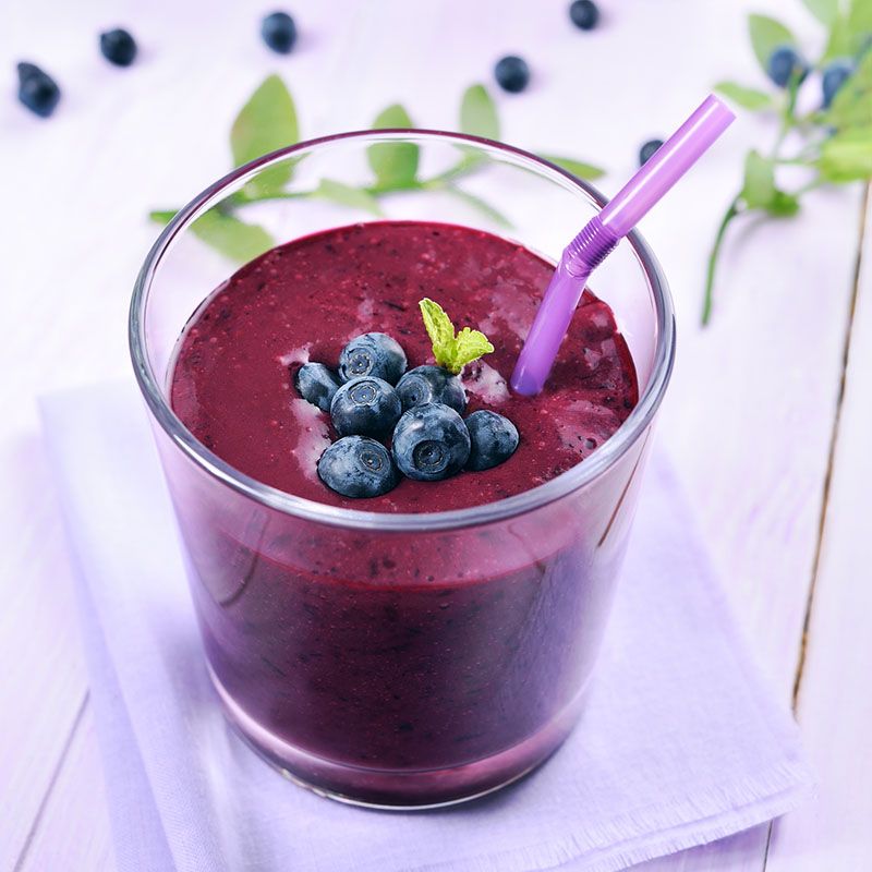 Glas mit lila Smoothie, Blaubeeren und Minze. Lila Trinkhalm. Auf weißem Untergrund.