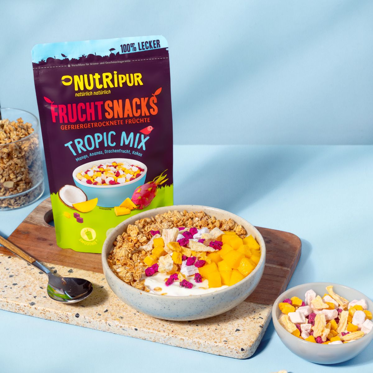 Schale mit Müsli und Früchten, daneben Beutel mit gefriergetrockneten Früchten. Aufschrift: NutriPur, Tropic Mix.