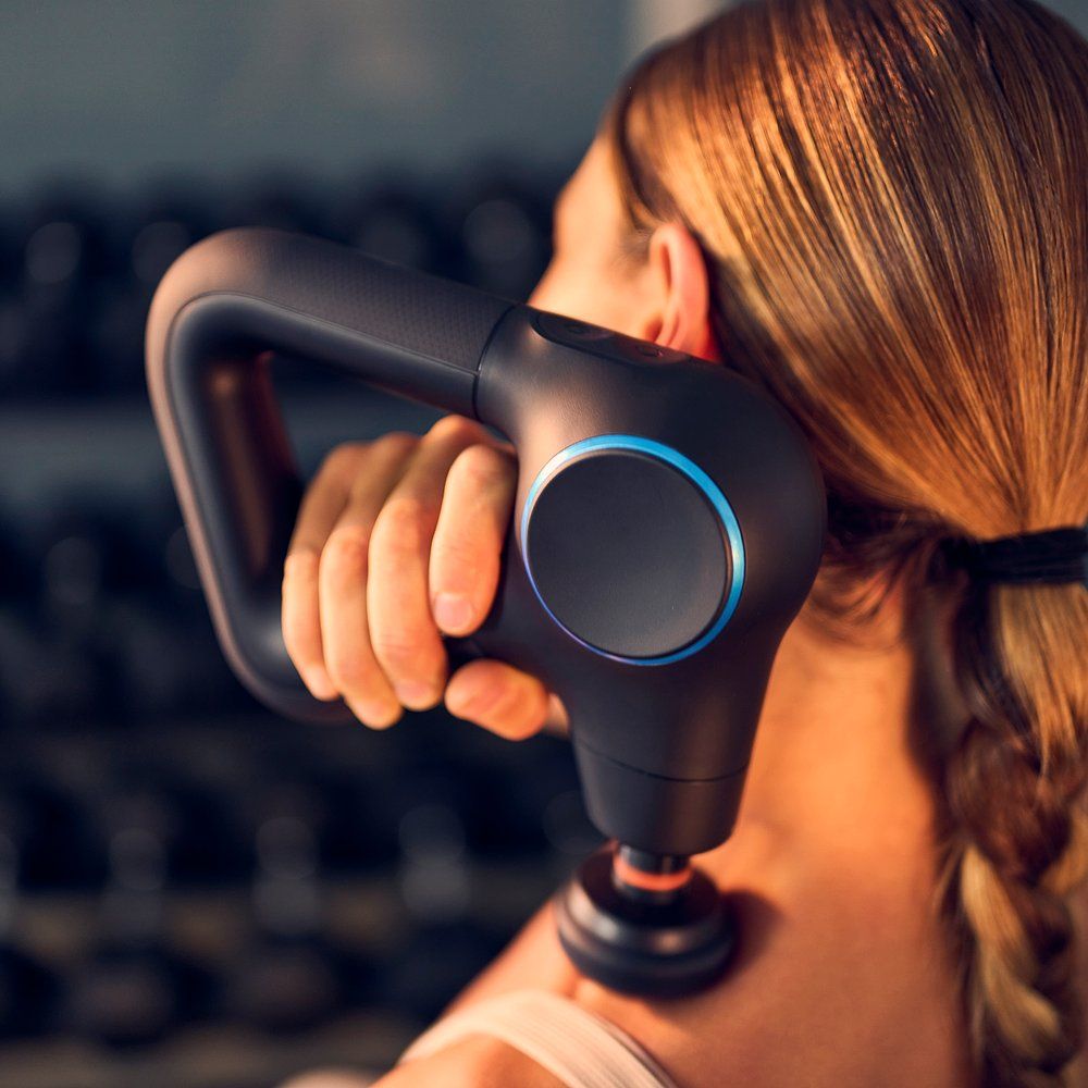 Person hält ein schwarzes Massagegerät am Rücken. Das Gerät hat einen blauen Ring und wird auf der Schulter verwendet.