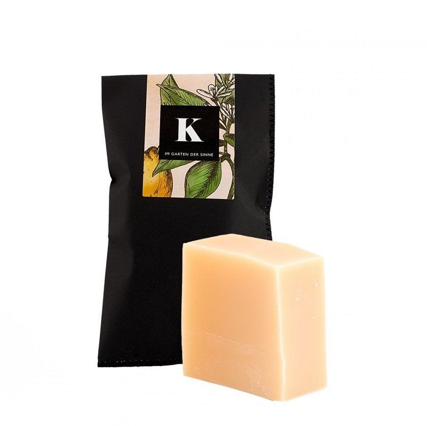 Beige Seife, rechteckig, neben schwarzer Verpackung mit Logo und Illustration. Text: Im Garten der Sinne.