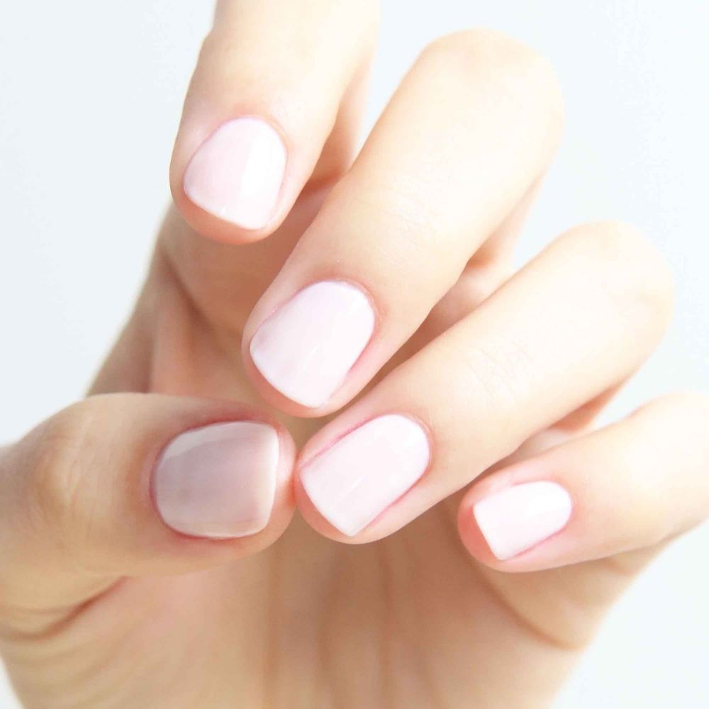 Hand mit hellrosa lackierten Fingernägeln. Die Nägel sind kurz und gleichmäßig gefeilt.