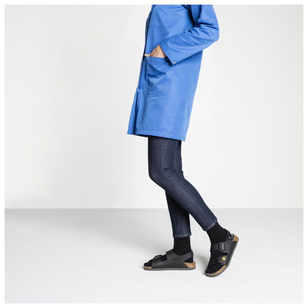 Person trägt schwarze Birkenstock Milano Sandalen. Person trägt blaue Jacke und Jeans.