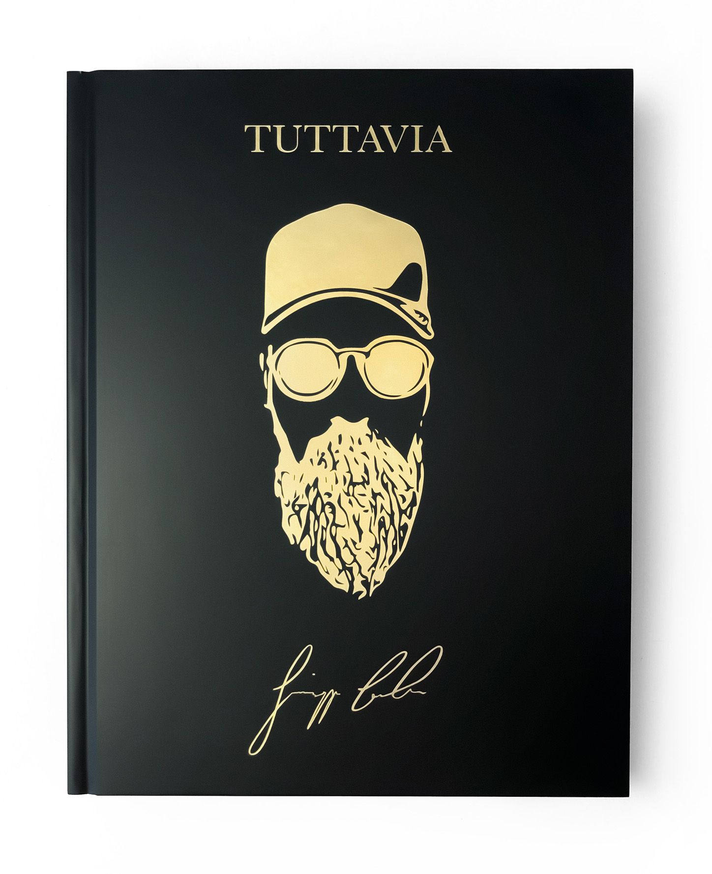 Schwarzes Buch mit goldenem Titel TUTTAVIA und goldener Illustration eines Mannes mit Bart, Brille und Mütze. Signatur.