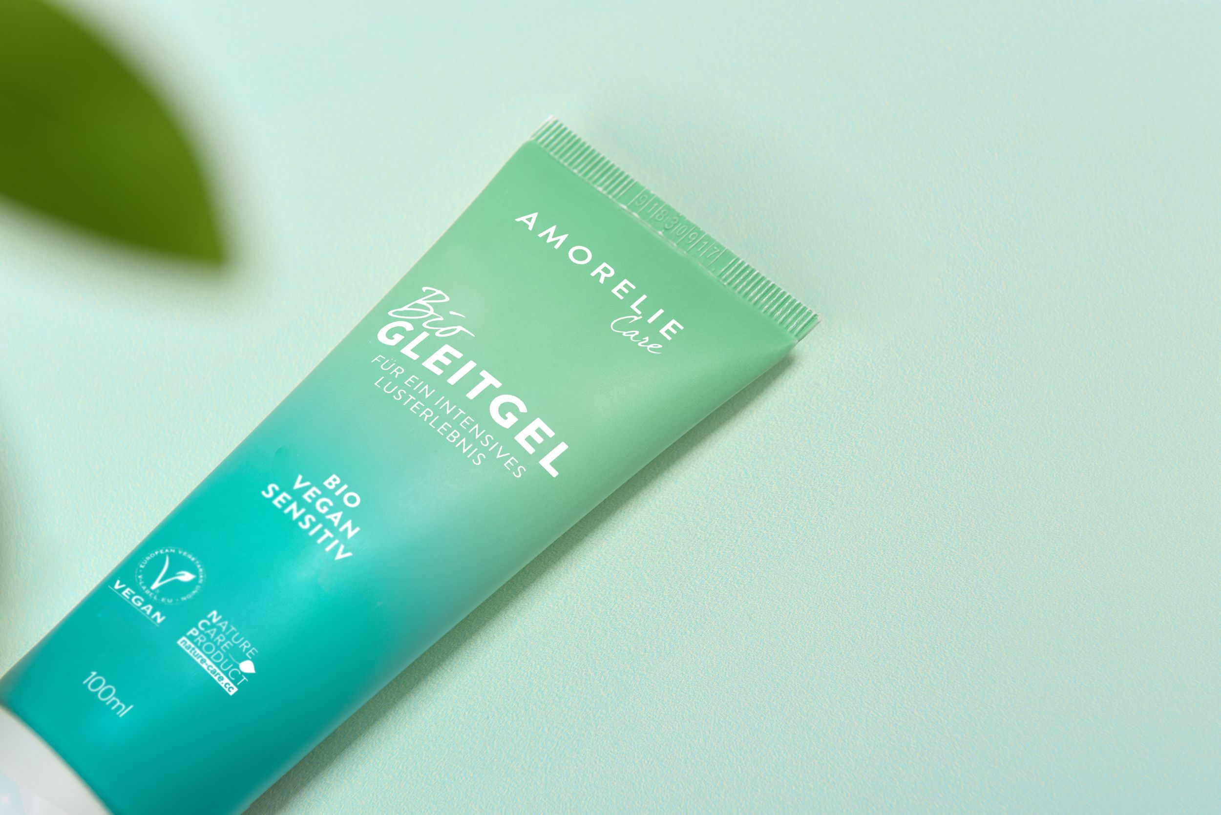 Gros plan d'un tube vert. Inscription: AMORELIE Care, Bio Gleitgel, Bio Vegan Sensitiv. Label Vegan. Fond vert.